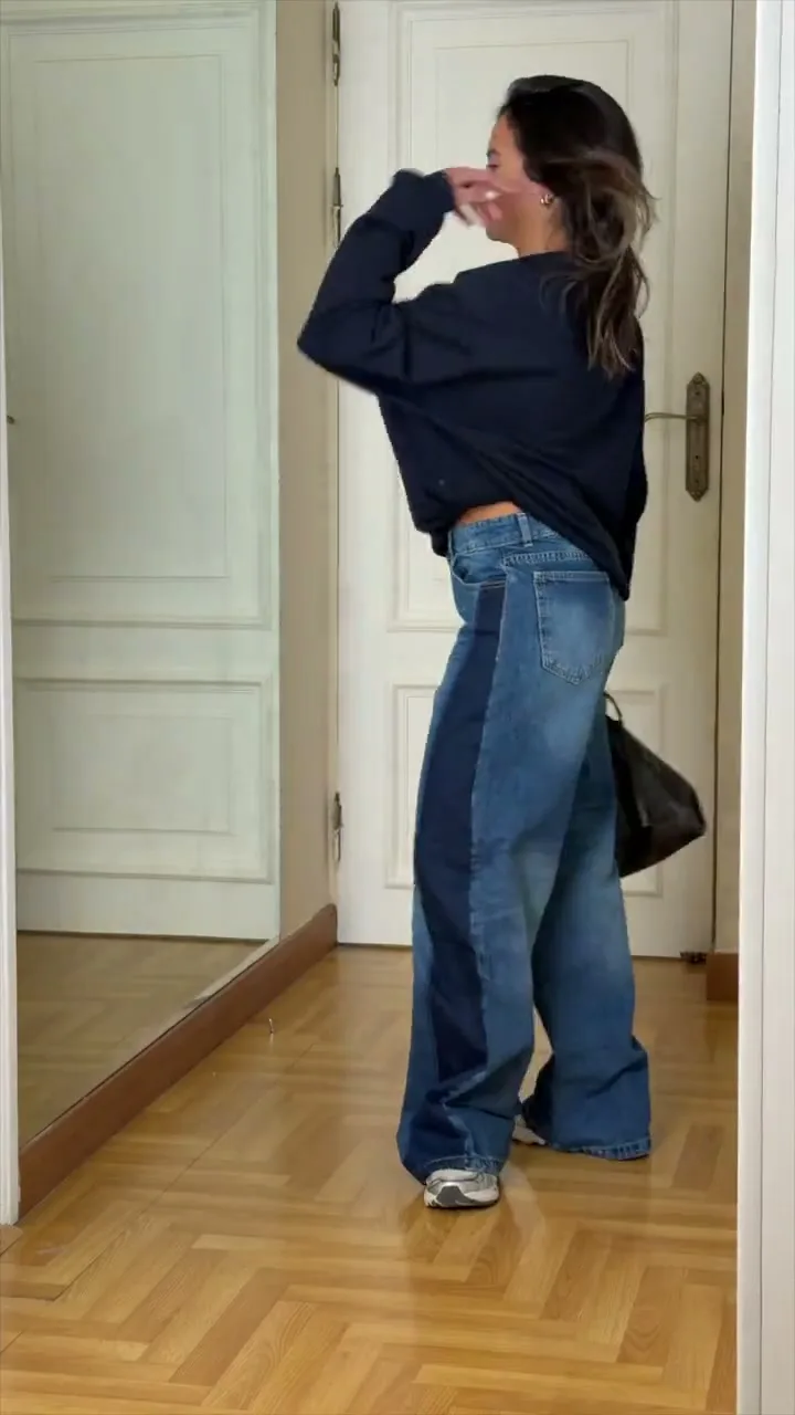 Model in a navy sweater and wide two-tone jeans indoors