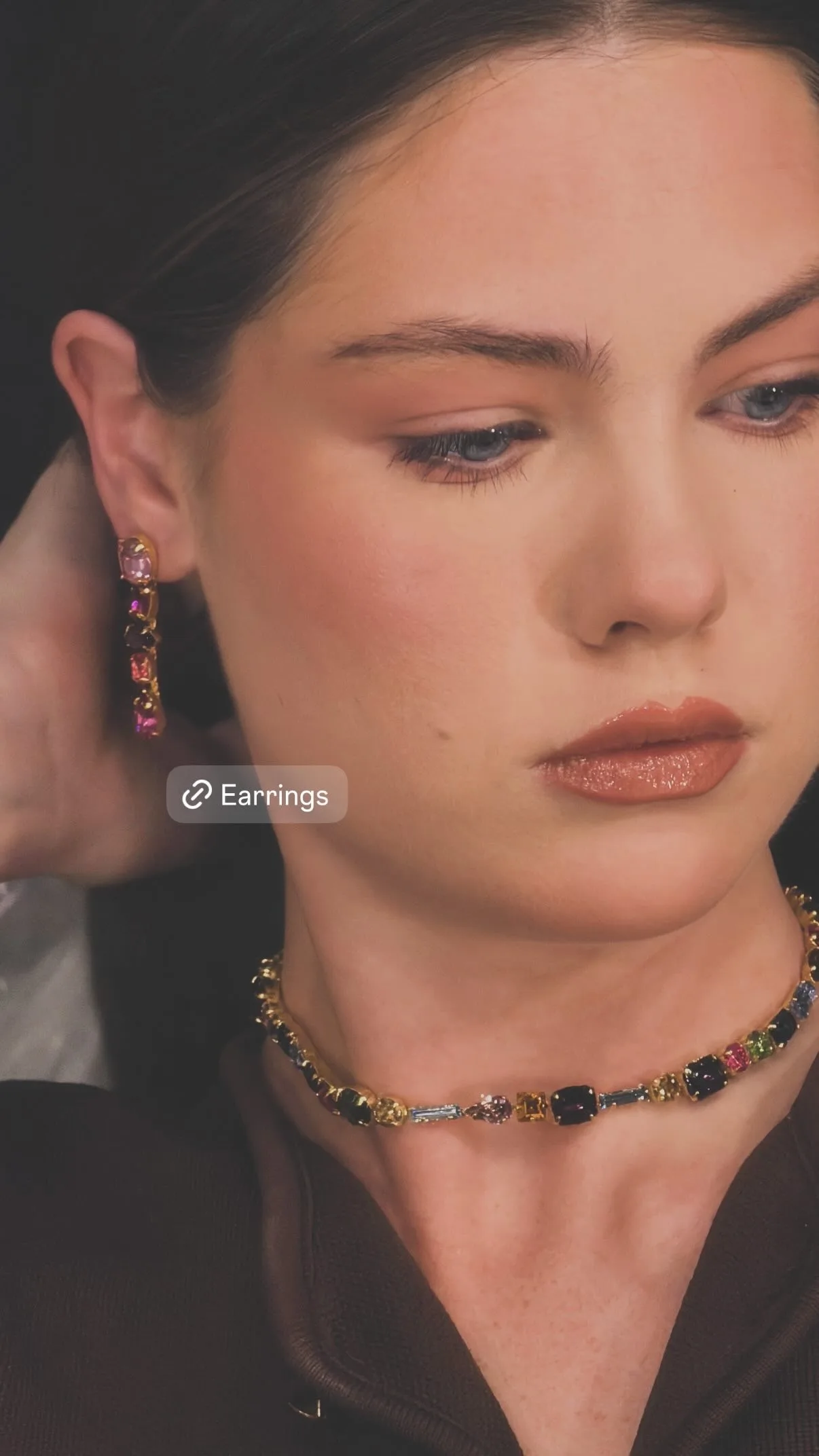 Model touching her hair, wearing pink drop earrings and a crystal necklace